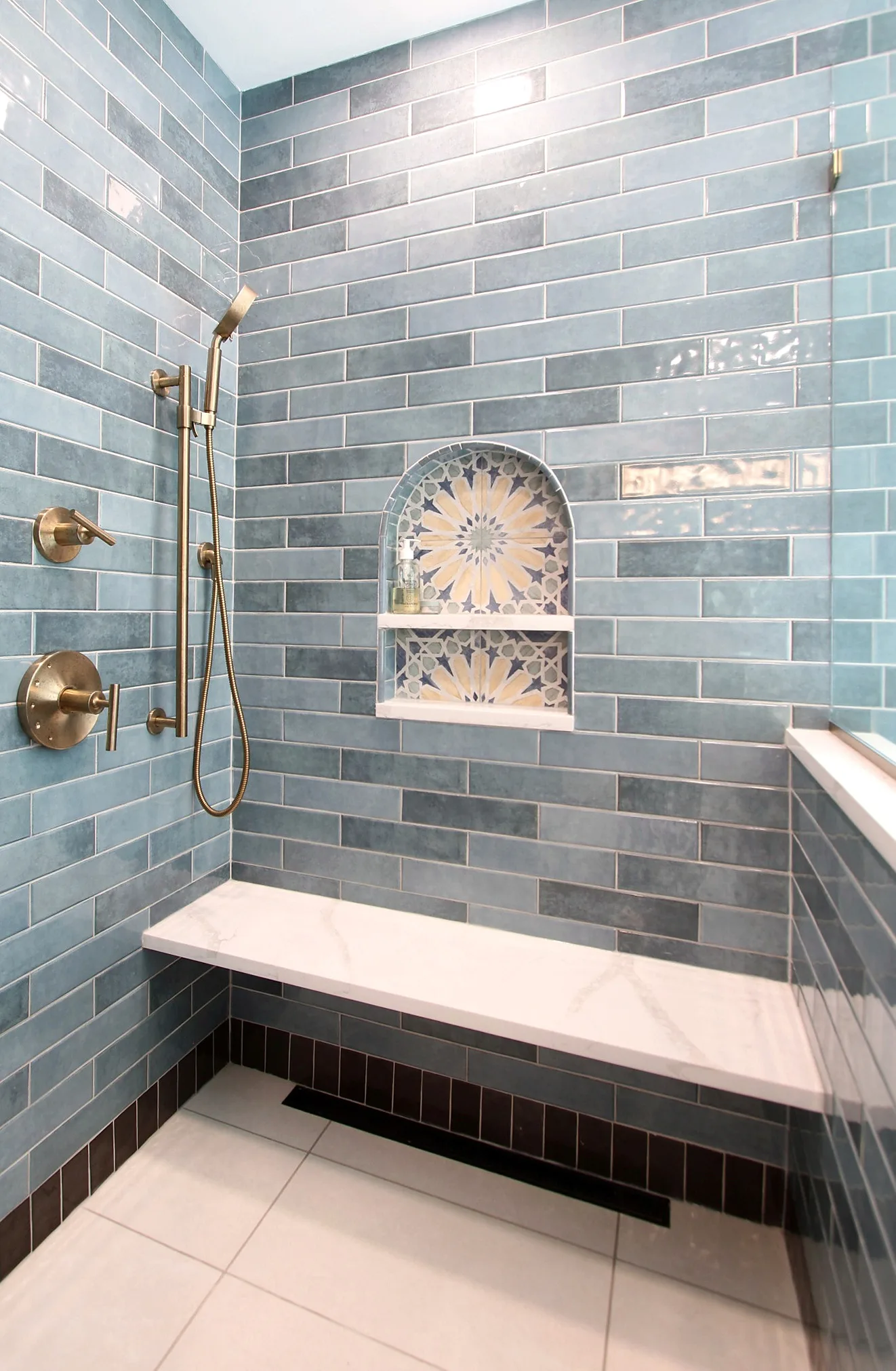 Large walk-in shower with blue-green tile, decorative niche, built-in bench and brass fixtures