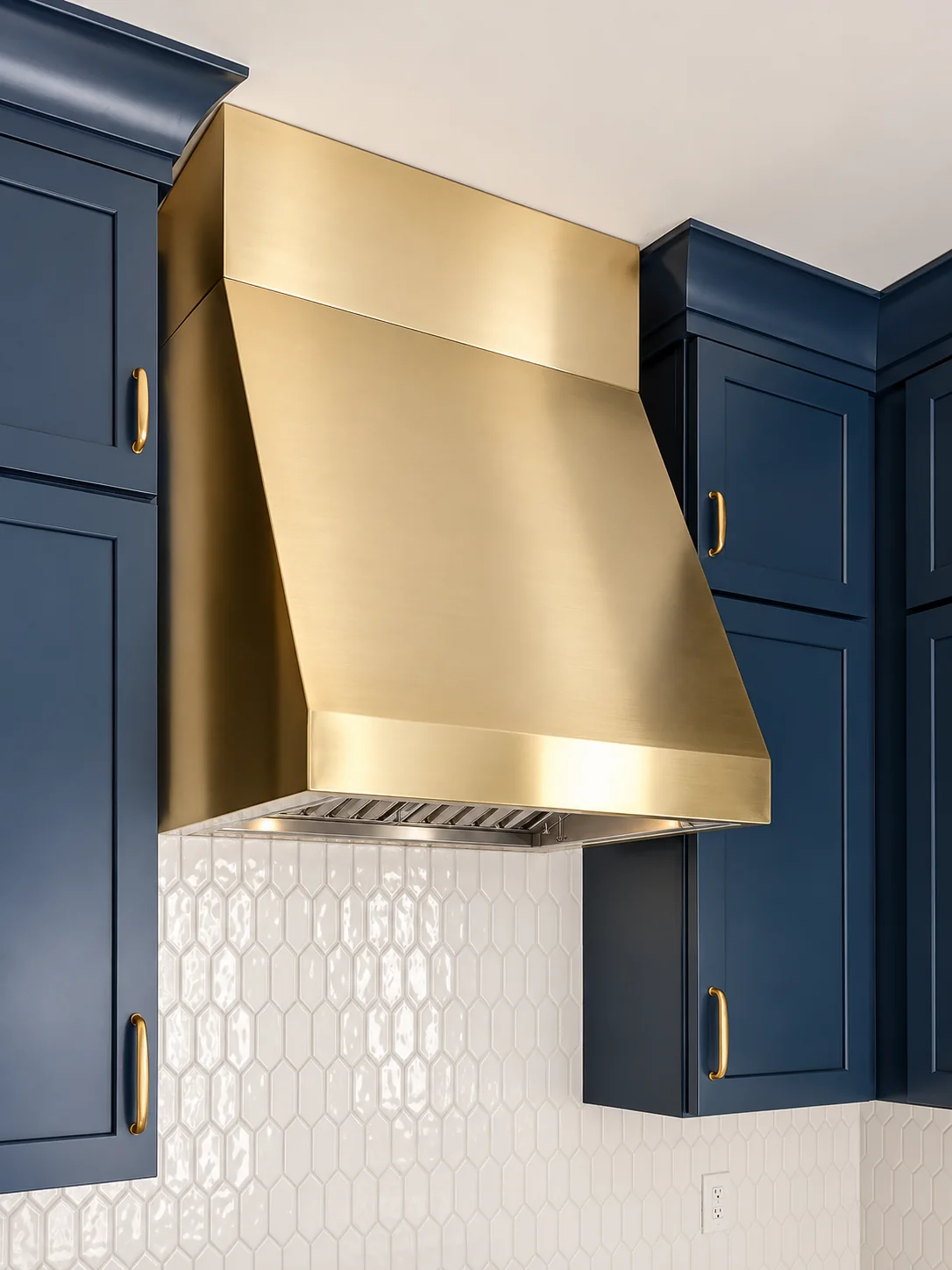 Blue kitchen cabinetry with custom brass range hood in a Melrose Park remodel by dRemodeling